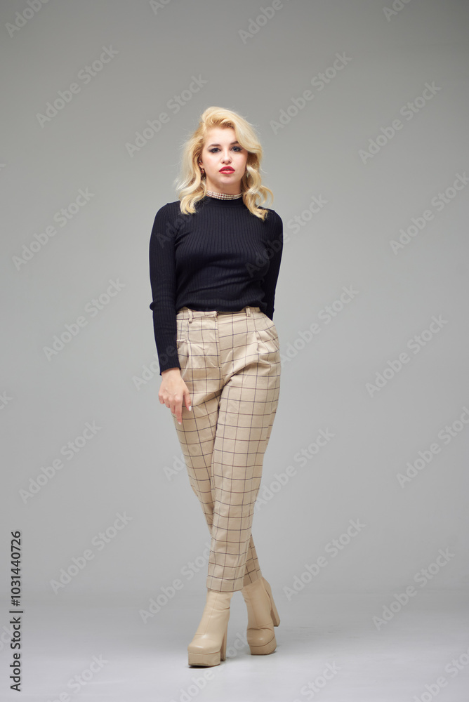 Beautiful girl with blond hair in a black sweater and brown pants posing in a studio on a gray background. Beautiful girl with blond hair in a black sweater and brown pants posing in a studio on a gray background.