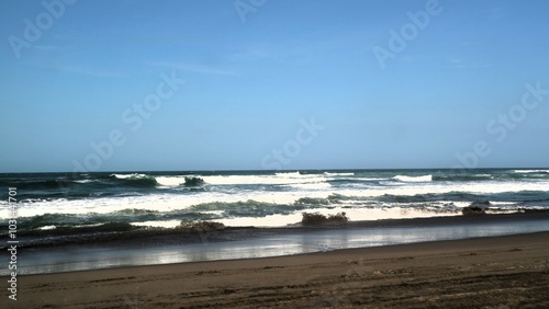 Waves crashing against the shore with a clear blue sky in the background at Parangtritis Beach, Yogyakarta.