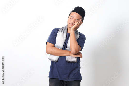 Portrait of exhausted Asian muslim man wearing sarung scarf sleeping with hand on head while standing. Isolated image on white background photo