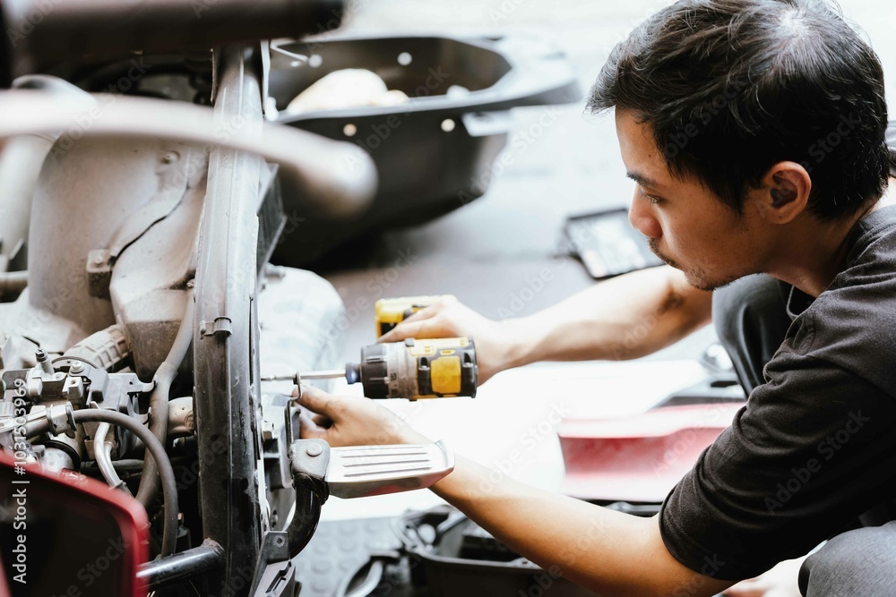 Motorcycle mechanic uses electric screwdriver ,power tool to repair motorcycle in garage,Checking and removing damaged motorcycle parts ,Maintenance and repair concept