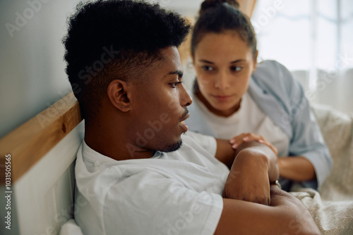 Pensive African American man being consoled by his girlfriend in bedroom.