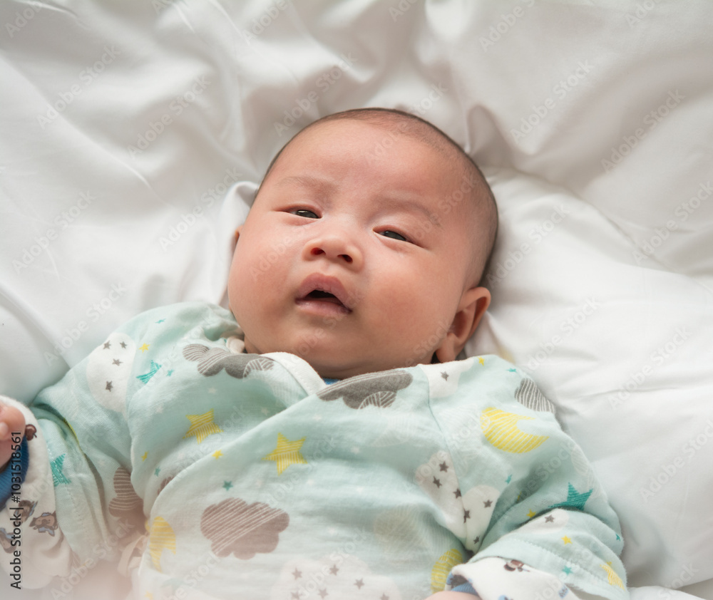 Close-up of male newborn baby wearing hat on his head with relaxed and happy smiling face lying on white bed. Close-up of male newborn baby wearing hat on his head with relaxed and happy smiling face lying on white bed.