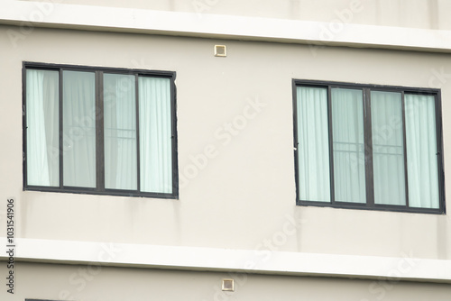 Two windows on a building with white walls and black frames. The windows are open and the curtains are drawn