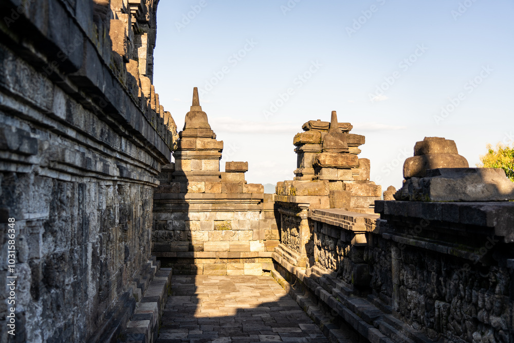 Naklejka premium Warm afternoon light from sunset hits carved Buddha statue, Stupa and stone wall relief at the ancient historical Buddhist UNESCO site of Borobudur (Barabudur), Magelang, Indonesia.
