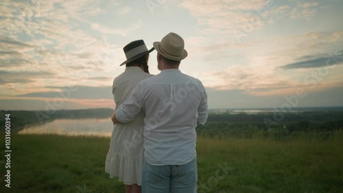Wallpaper Mural Close-up of lovers standing on a grassy hill at sunset, gazing at the sky. The man, dressed in a white shirt, hat, and jeans, gently holds the woman by the waist. She wears a hat and a white dress Torontodigital.ca
