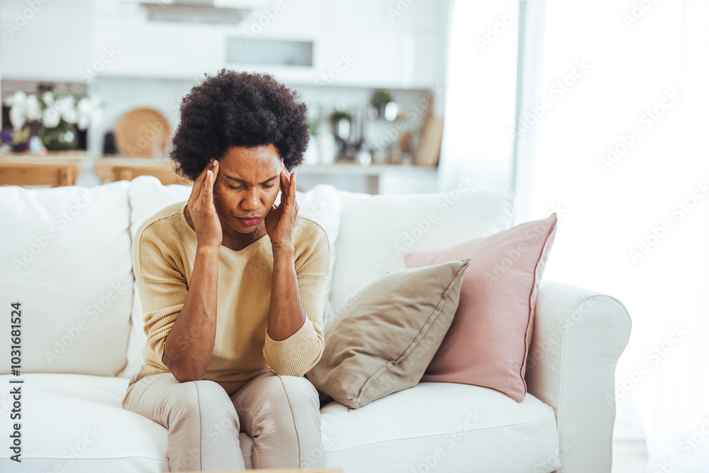 Woman Sitting On Sofa Experiencing Stress And Headache At Home Woman Sitting On Sofa Experiencing Stress And Headache At Home