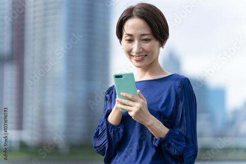 ビル街でスマートフォンを操作している女性 photo