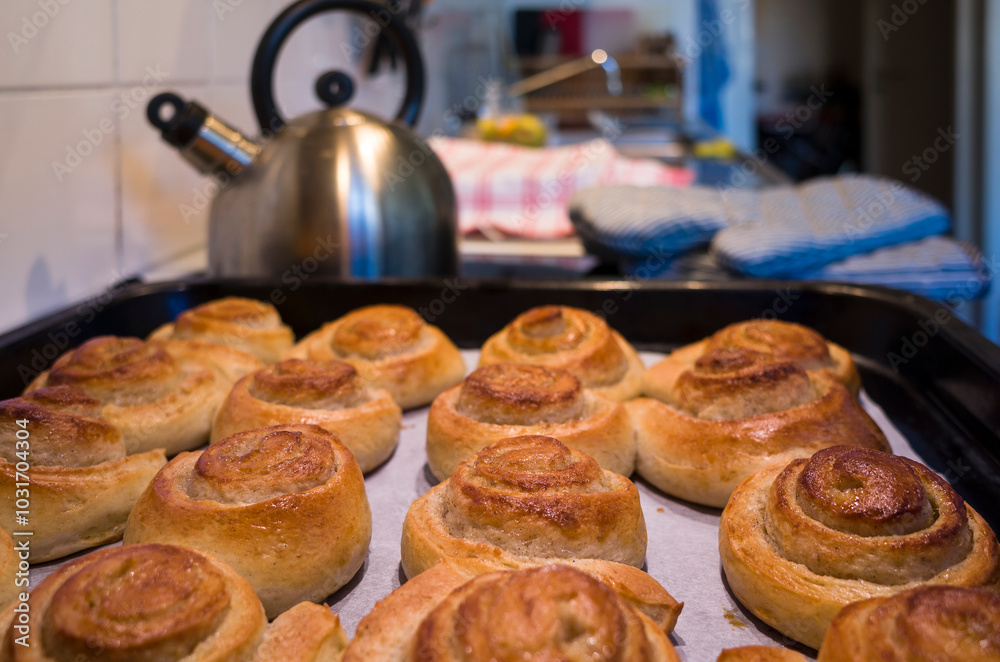 Freshly baked buns rolls on a baking sheet on baking paper, Swedish traditional pastry kanelbulle, Selective focus photo with teapot on kitchen table blurred on background Freshly baked buns rolls on a baking sheet on baking paper, Swedish traditional pastry kanelbulle, Selective focus photo with teapot on kitchen table blurred on background
