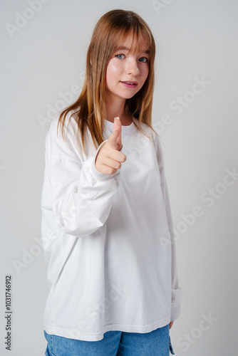 Young girl in a white sweater pointing against a plain background