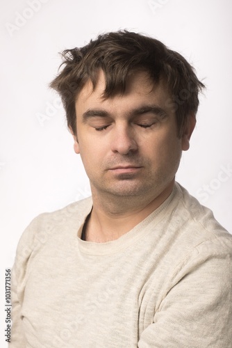 Portrait of a man with his eyes closed, wearing a light beige sweater, against a plain white background. The calm expression on his face conveys a sense of peace and relaxation