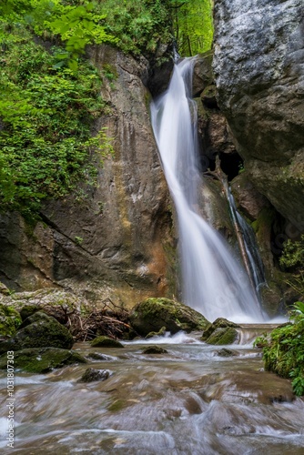 Vertical view of a stunning waterfall cascading down a rocky cliff surrounded by lush greenery