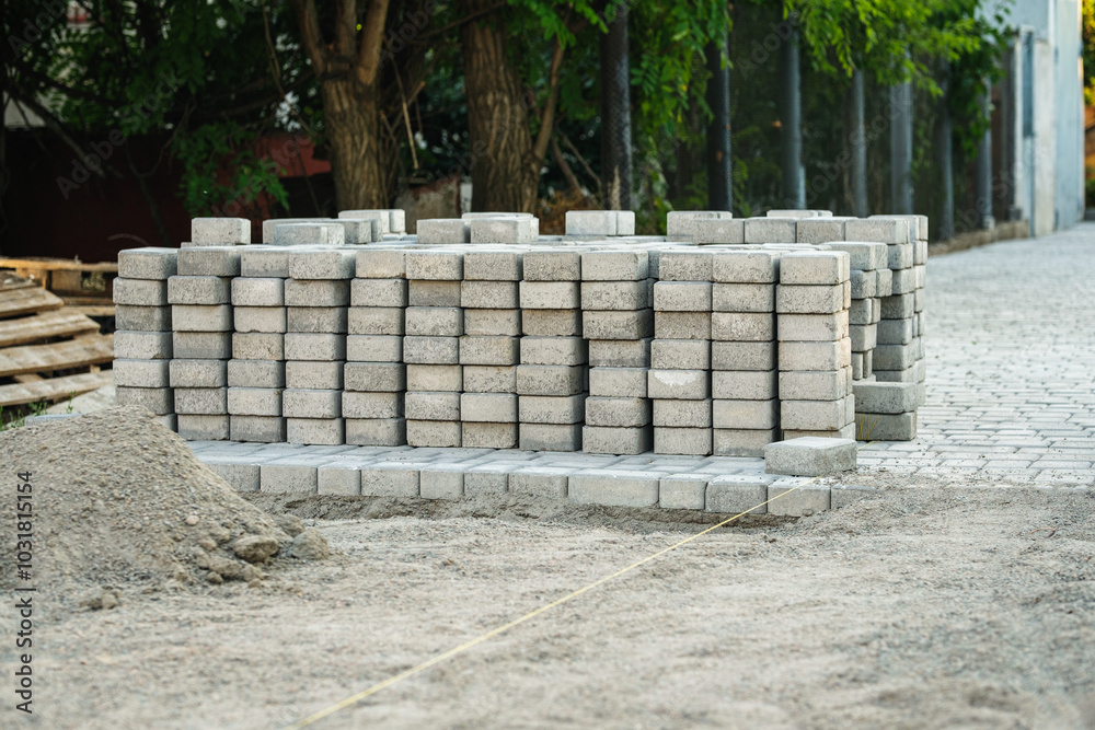 Workers are preparing to build a new path by carefully arranging gray bricks along a serene street, illuminated by soft evening light and surrounded by greenery. Workers are preparing to build a new path by carefully arranging gray bricks along a serene street, illuminated by soft evening light and surrounded by greenery.