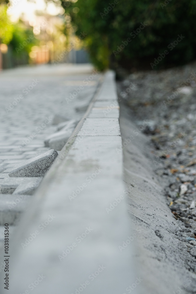 A close-up view of uneven paving stones next to a curb in a park setting shows the wear and tear that calls for repair work, as sunlight illuminates the area. A close-up view of uneven paving stones next to a curb in a park setting shows the wear and tear that calls for repair work, as sunlight illuminates the area.