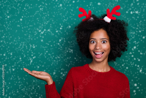 Photo of funny impressed little school girl dressed red sweater horns holding arm empty space isolated green color background photo