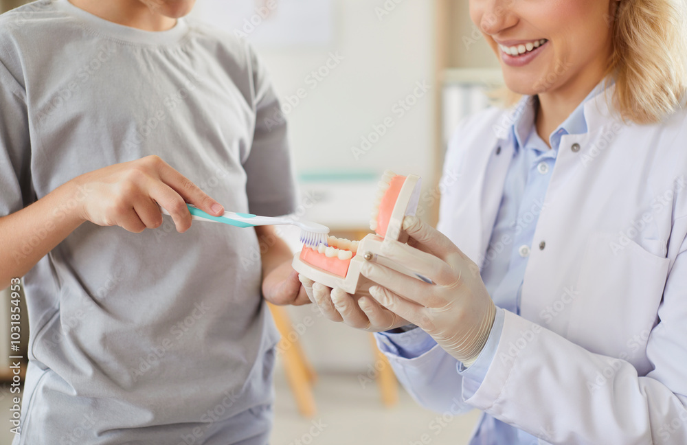 Young smiling woman stomatologist teaching cleaning teeth a little child boy patient for oral health in hospital. Professional dentist teaching how to use toothbrush in dental office. Young smiling woman stomatologist teaching cleaning teeth a little child boy patient for oral health in hospital. Professional dentist teaching how to use toothbrush in dental office.
