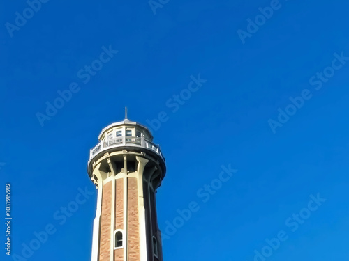 A lighthouse is tall and white with a blue sky in the background. The lighthouse is the focal point of the image, and the blue sky creates a sense of calm and serenity