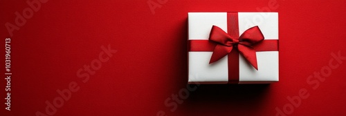A beautifully wrapped white gift box with a red ribbon resting on a vibrant r...