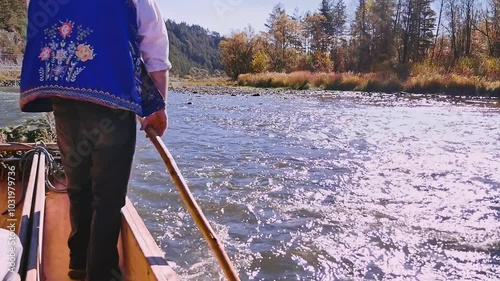 Raftsman wearing traditional clothing rowing a raft with tourists along beautiful Dunajec river gorge on a sunny autumn day, Poland photo