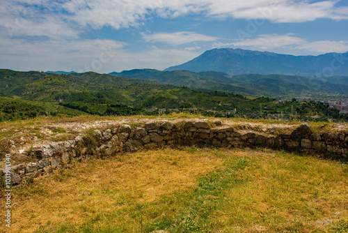 The June landscape around the historic town of Berat in southern Albania. Viewed from Berat Castle with part of the castle walls foreground. A picturesque rural landscape of olive groves, pine trees