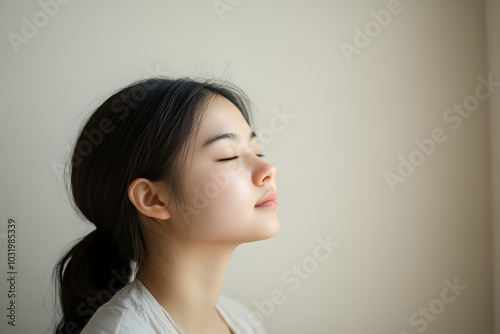 A minimalist photograph of an Asian girl with closed eyes, expressing tranquility and serenity in soft natural light