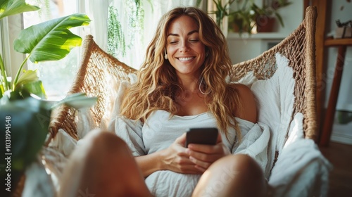 Relaxing and smiling, a woman enjoys her time in a boho-inspired cozy hammock, surrounded by lush greenery, capturing a serene and comfortable moment indoors. photo