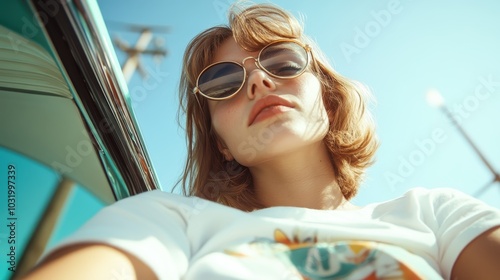 A fashionable young woman wearing stylish sunglasses is enjoying a drive, basking in the warmth of a sunny day, as captured from an interesting low angle. photo