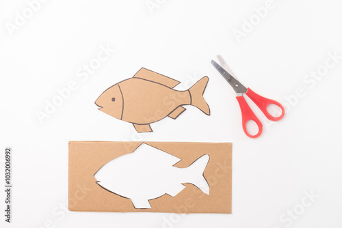 simple craft activity involving cutting shapes from cardboard, which can be used for educational or creative purposes. cut out fish shape itself, a pair of red handled scissors, step in DIY process photo