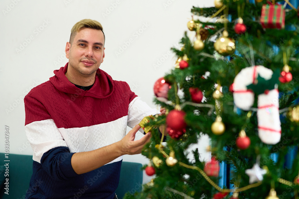 Young man smiling and decorating Christmas tree at home Young man smiling and decorating Christmas tree at home