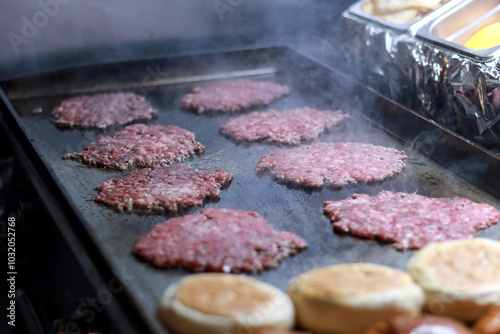Smash burgers cooking on a hot grill in a busy restaurant kitchen, buns toasting nearby