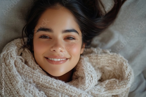 Top view of happy latin woman lying under blanket on soft pillow in bed, looking and smiling at camera, having fun at home, Generative AI