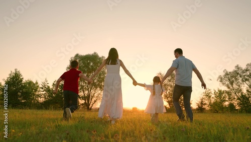 Happy family holding hands running towards sun and having fun in city park at sunset. Slow motion. Family, mom, dad daughter run together, happy childhood, freedom people, future, family game concept photo