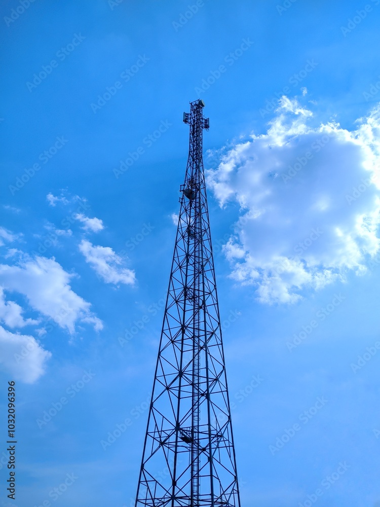 The tall communications tower stands against a bright blue sky with fluffy white clouds. The tower has many antennas at the top and stairs on the sides. The tall communications tower stands against a bright blue sky with fluffy white clouds. The tower has many antennas at the top and stairs on the sides.