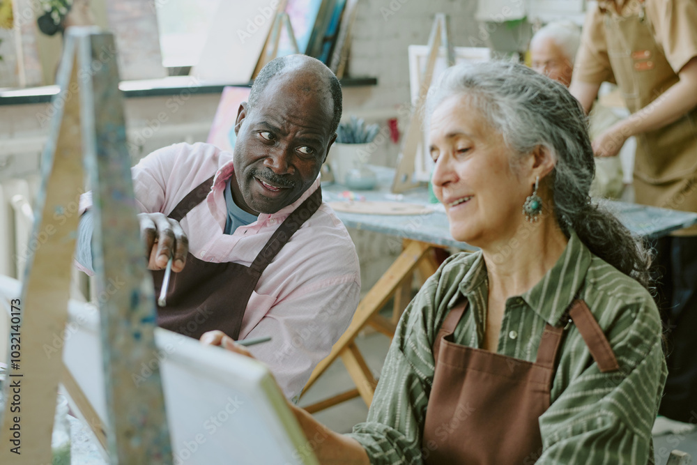 High angle shot of African American husband pointing to canvas while giving advices to his beloved Caucasian wife High angle shot of African American husband pointing to canvas while giving advices to his beloved Caucasian wife