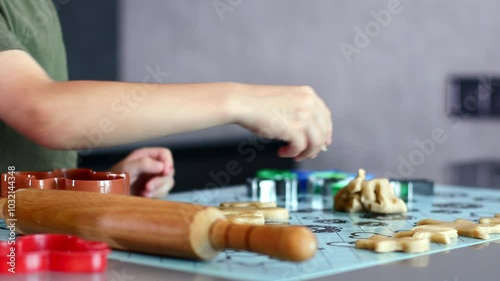 Close up of little boy hands making cookies using cookie cutters and dough in the kitchen at home.