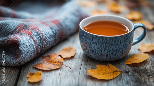 A cozy autumn setup with a plaid blanket, a cup of hot spiced cider, and dried leaves scattered across a rustic wooden table.