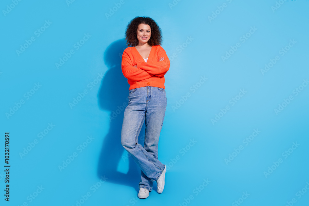 Photo portrait of wavy haired model confident posing woman wearing orange cardigan and jeans isolated on blue color background Photo portrait of wavy haired model confident posing woman wearing orange cardigan and jeans isolated on blue color background