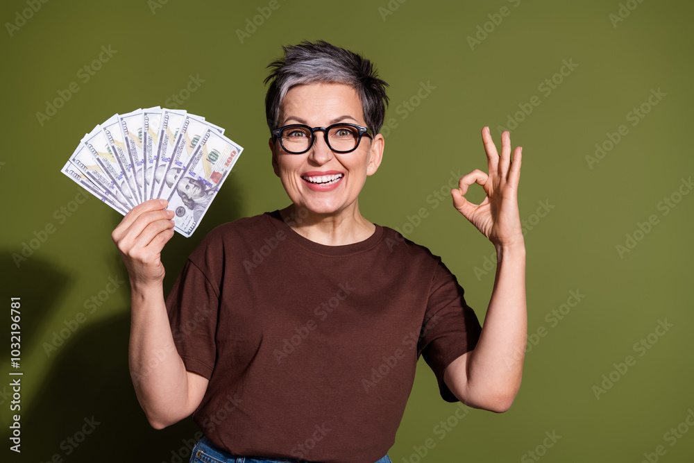Portrait of pretty aged lady money okey symbol wear brown t-shirt isolated on khaki color background Portrait of pretty aged lady money okey symbol wear brown t-shirt isolated on khaki color background