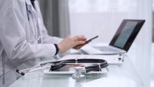 Stethoscope and clipboard are lying on the glass table while doctor woman is using a smartphone at the background. Medicine concept