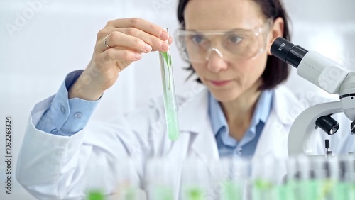 Woman scientist with protective glasses examining lab tube with a green fluid. Microbiology and science concept