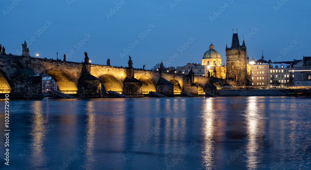 A scenic view of the historic Charles Bridge in Prague illuminated at dusk, with its stone arches and statues reflecting in the calm waters of the Vltava River A scenic view of the historic Charles Bridge in Prague illuminated at dusk, with its stone arches and statues reflecting in the calm waters of the Vltava River