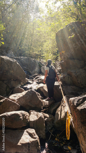  Young woman hiking in a green forest surrounded by big rocks, on a warm spring afternoon   