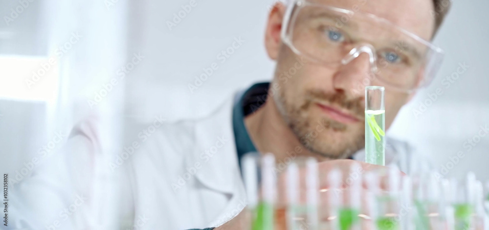 Man researcher with safety glasses is examining lab tube with a green fluid in a modern laboratory, close-up. Science, microbiology and medicine Man researcher with safety glasses is examining lab tube with a green fluid in a modern laboratory, close-up. Science, microbiology and medicine