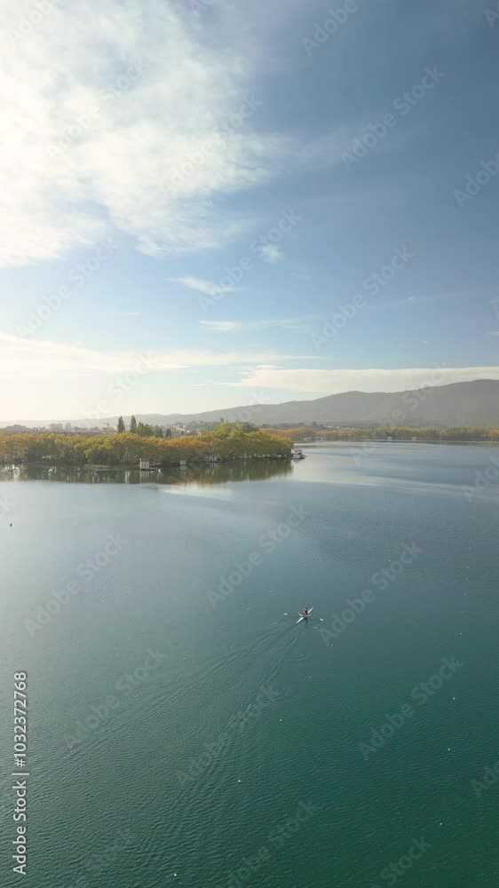 a serene lake surrounded by forested areas and distant mountains under a clear blue sky. A single person in a small boat is in the middle of the lake. a serene lake surrounded by forested areas and distant mountains under a clear blue sky. A single person in a small boat is in the middle of the lake.