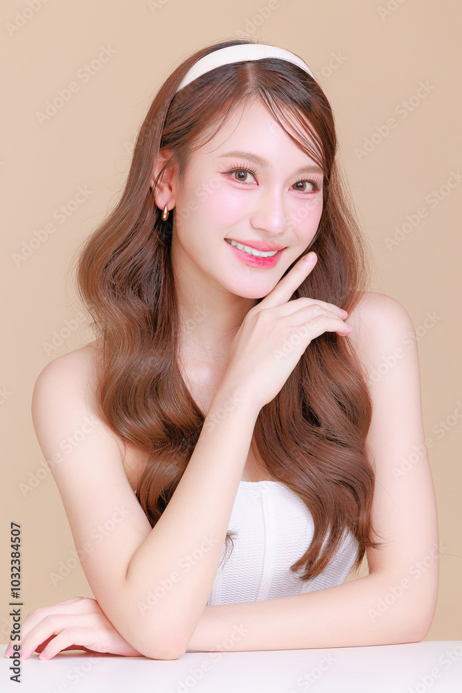 Pretty Asian beauty woman curly long hair with Korean makeup glowing face and healthy facial skin portrait smile on isolated beige background. Cosmetology ,Plastic surgery. Pretty Asian beauty woman curly long hair with Korean makeup glowing face and healthy facial skin portrait smile on isolated beige background. Cosmetology ,Plastic surgery.