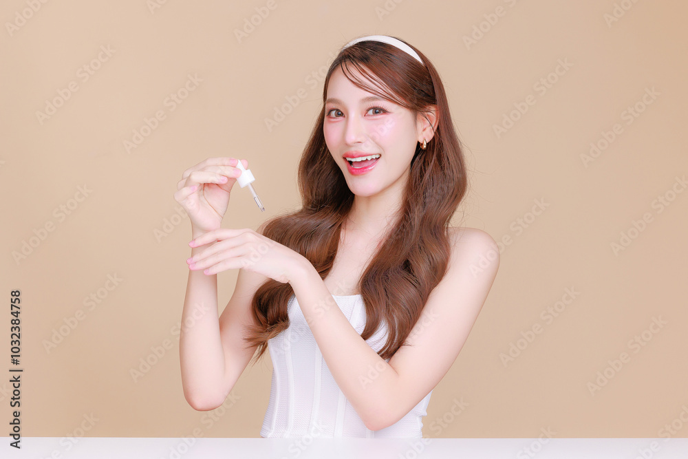 Pretty Asian beauty woman curly long hair with Korean makeup glowing face and healthy facial skin portrait smile holding dropper apply serum on isolated beige background. Cosmetology ,Plastic surgery. Pretty Asian beauty woman curly long hair with Korean makeup glowing face and healthy facial skin portrait smile holding dropper apply serum on isolated beige background. Cosmetology ,Plastic surgery.