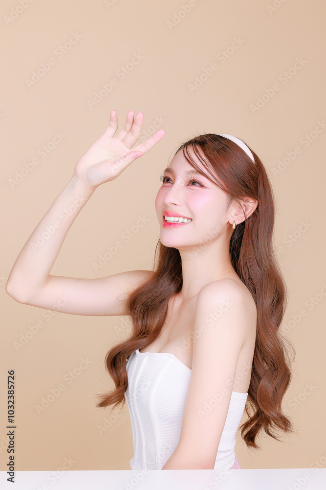 Pretty Asian beauty woman curly long hair with Korean makeup glowing face and healthy facial skin portrait smile on isolated beige background. Cosmetology ,Plastic surgery. Pretty Asian beauty woman curly long hair with Korean makeup glowing face and healthy facial skin portrait smile on isolated beige background. Cosmetology ,Plastic surgery.