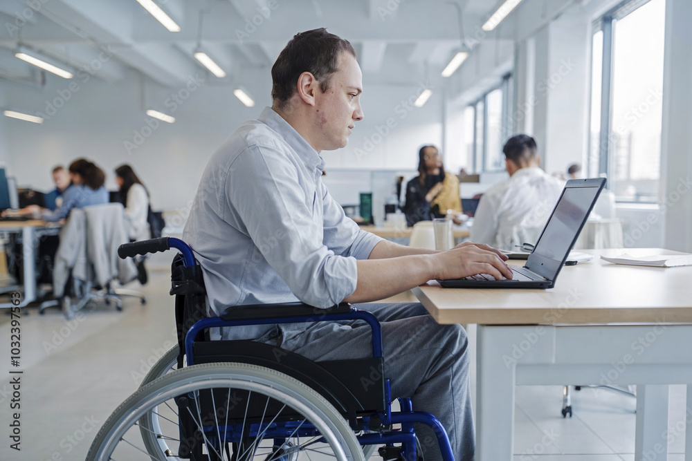 Disabled man sits in a wheelchair and works in an office on a laptop. Disabled man sits in a wheelchair and works in an office on a laptop.