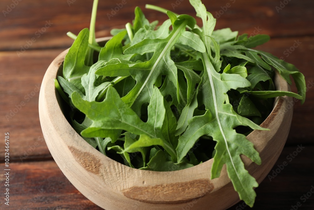 Fresh green arugula leaves in bowl on wooden table, closeup Fresh green arugula leaves in bowl on wooden table, closeup