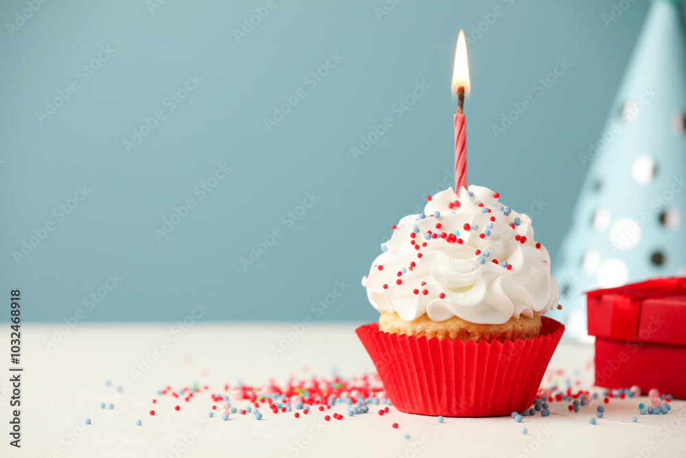 Birthday cupcake with burning candle, gift and party cone on white table. Space for text Birthday cupcake with burning candle, gift and party cone on white table. Space for text