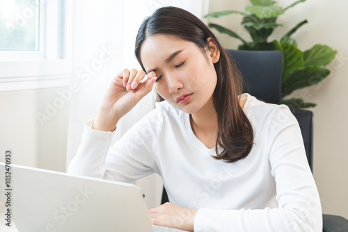 Tired asian young woman burnout, stressed from problem work at desk in office, looking at laptop computer, feeling sick, pain eye strain rubbing dry irritated eyes fatigued working late on deadline.